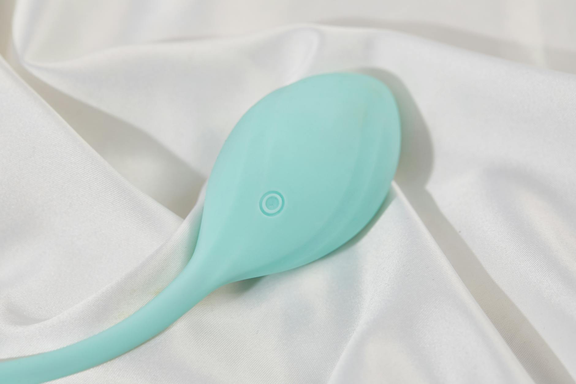 A teal clitoral vibrator resting on soft white fabric, symbolizing gentle pleasure and intimate wellness
