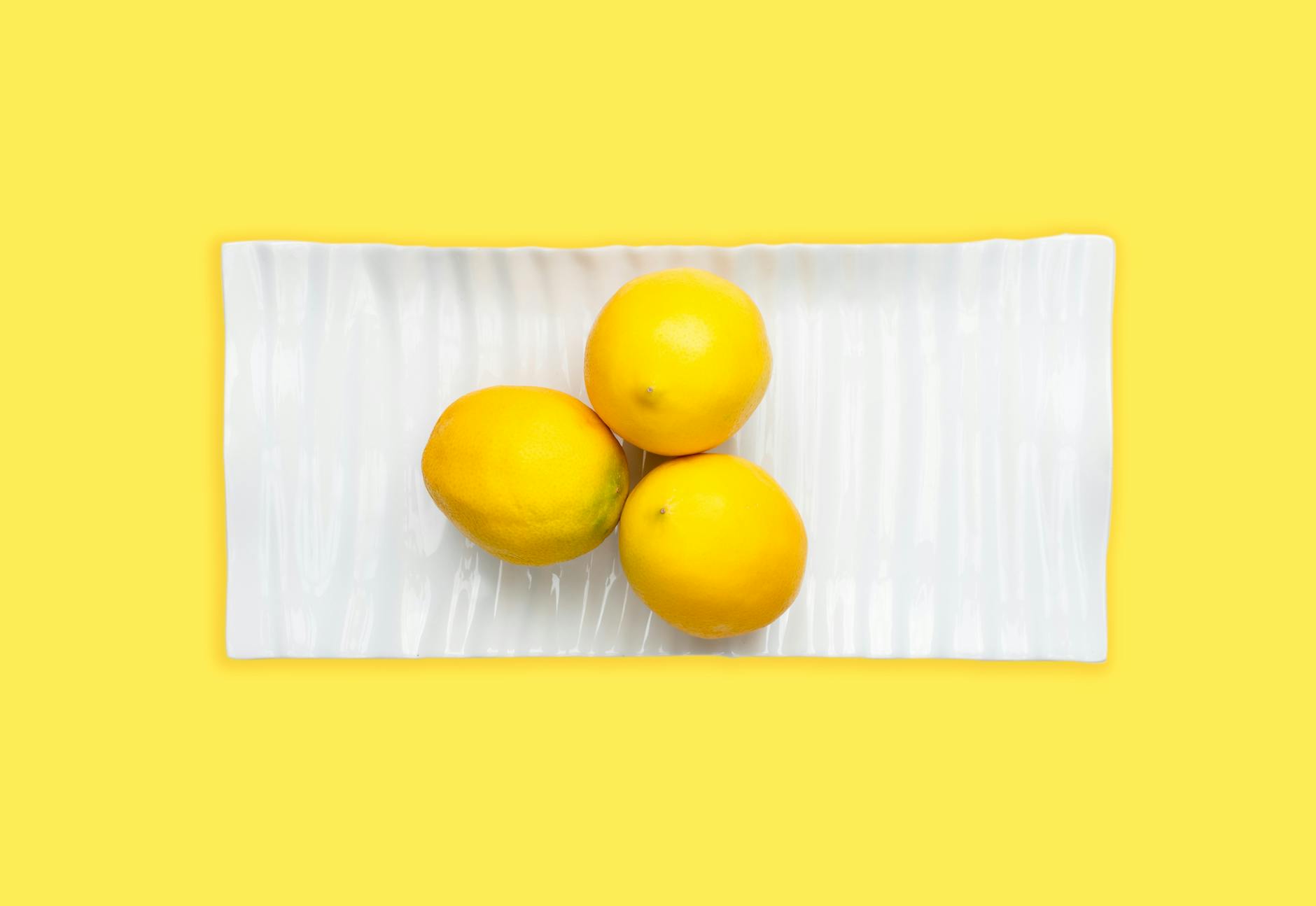 Bright yellow silicone lemon vibrator surrounded by peeled bananas on a sunny yellow background