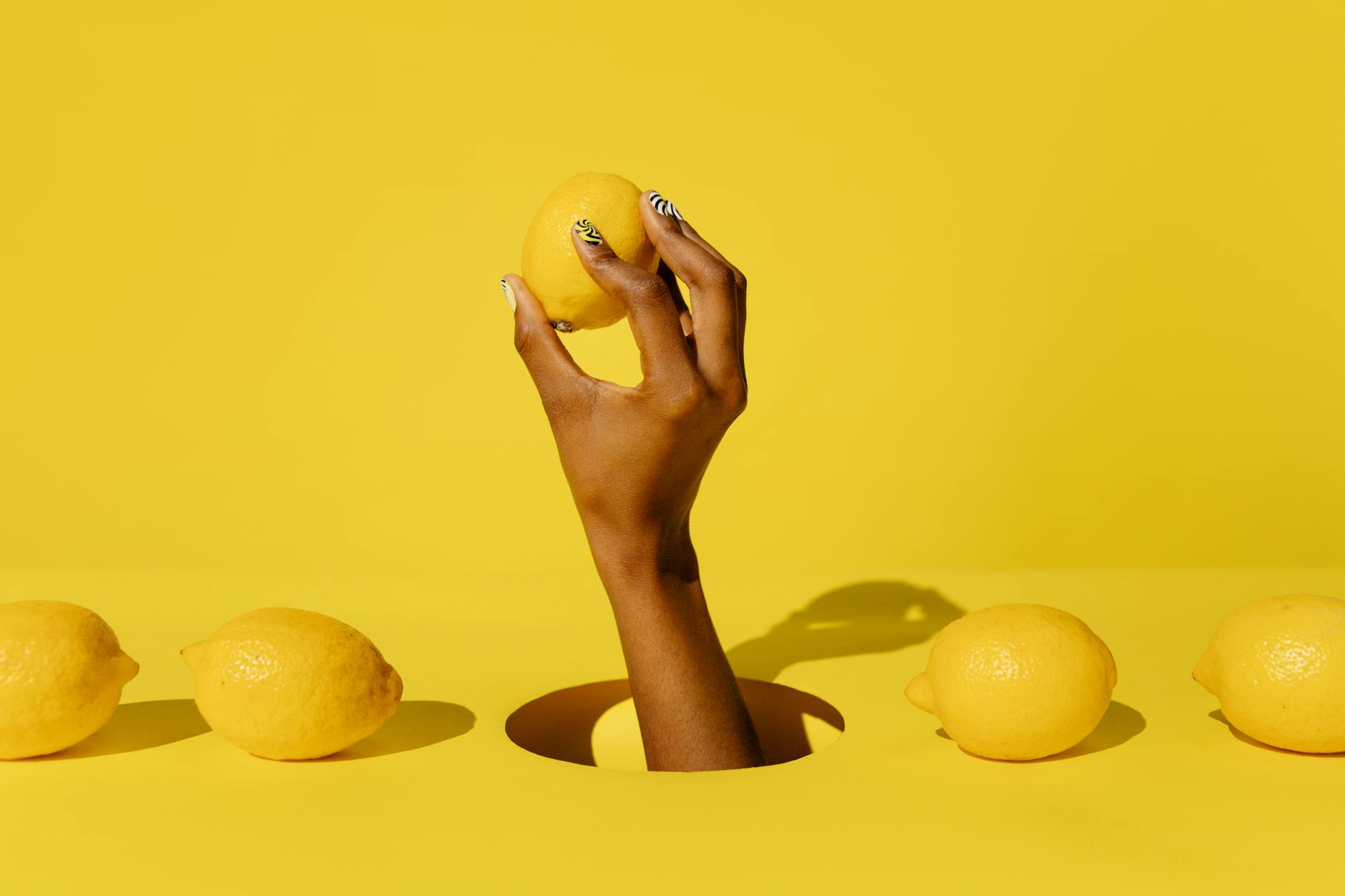A hand holding a fresh lemon against a vivid yellow background, symbolizing the simplicity and confidence of Hello Nancy's lemon clitoral vibrator design.
