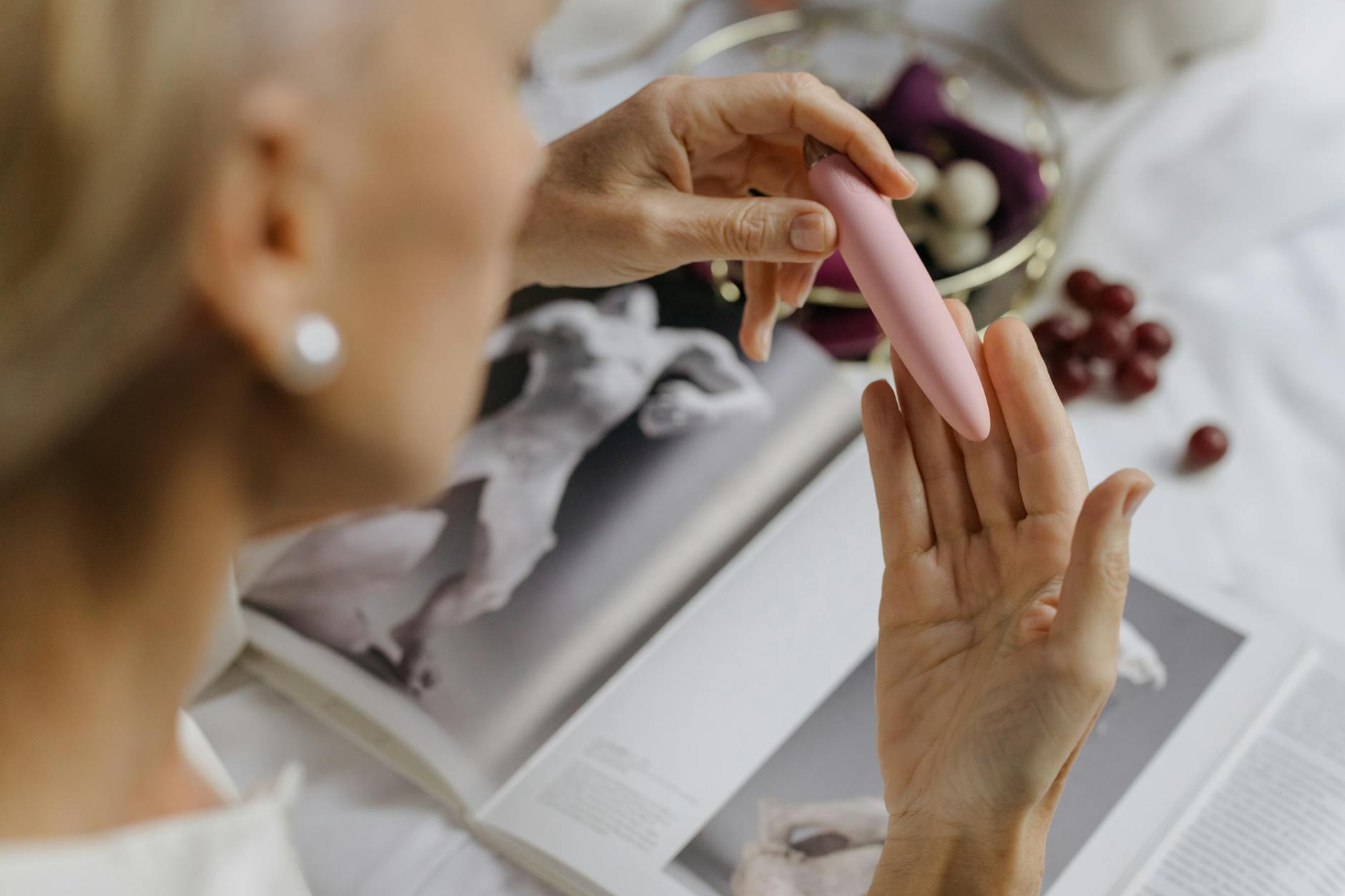 Woman holding a pink clitoral vibrator with art books in background, symbolizing intimate self-discovery and pleasure