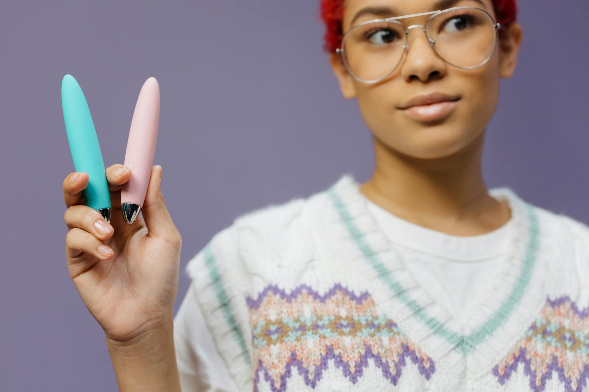 Close-up of hands holding colorful clitoral vibrators against a purple background