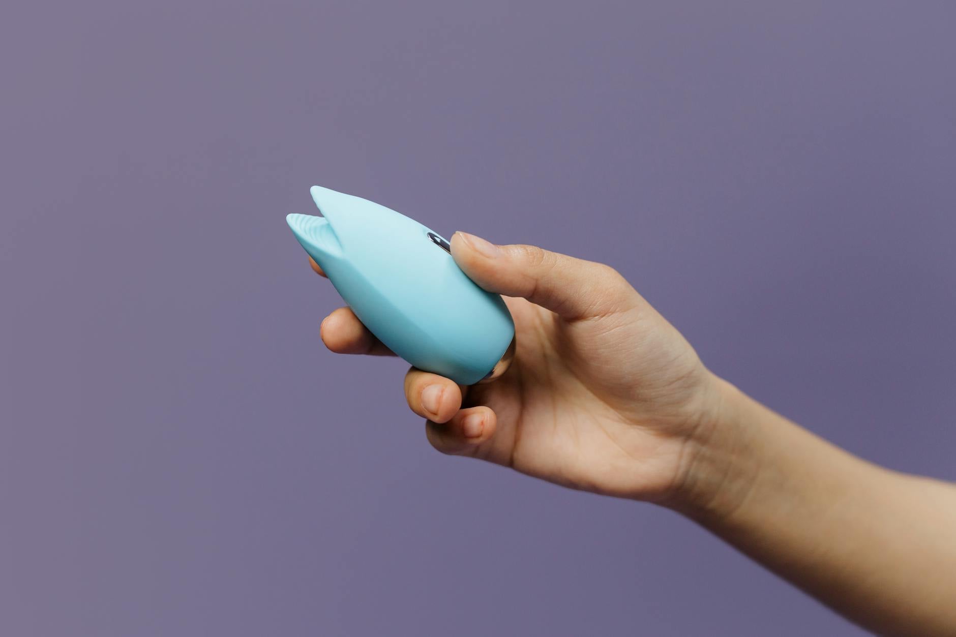 Manos sosteniendo un vibrador azul contra un fondo púrpura, promoviendo el amor propio y la sexualidad