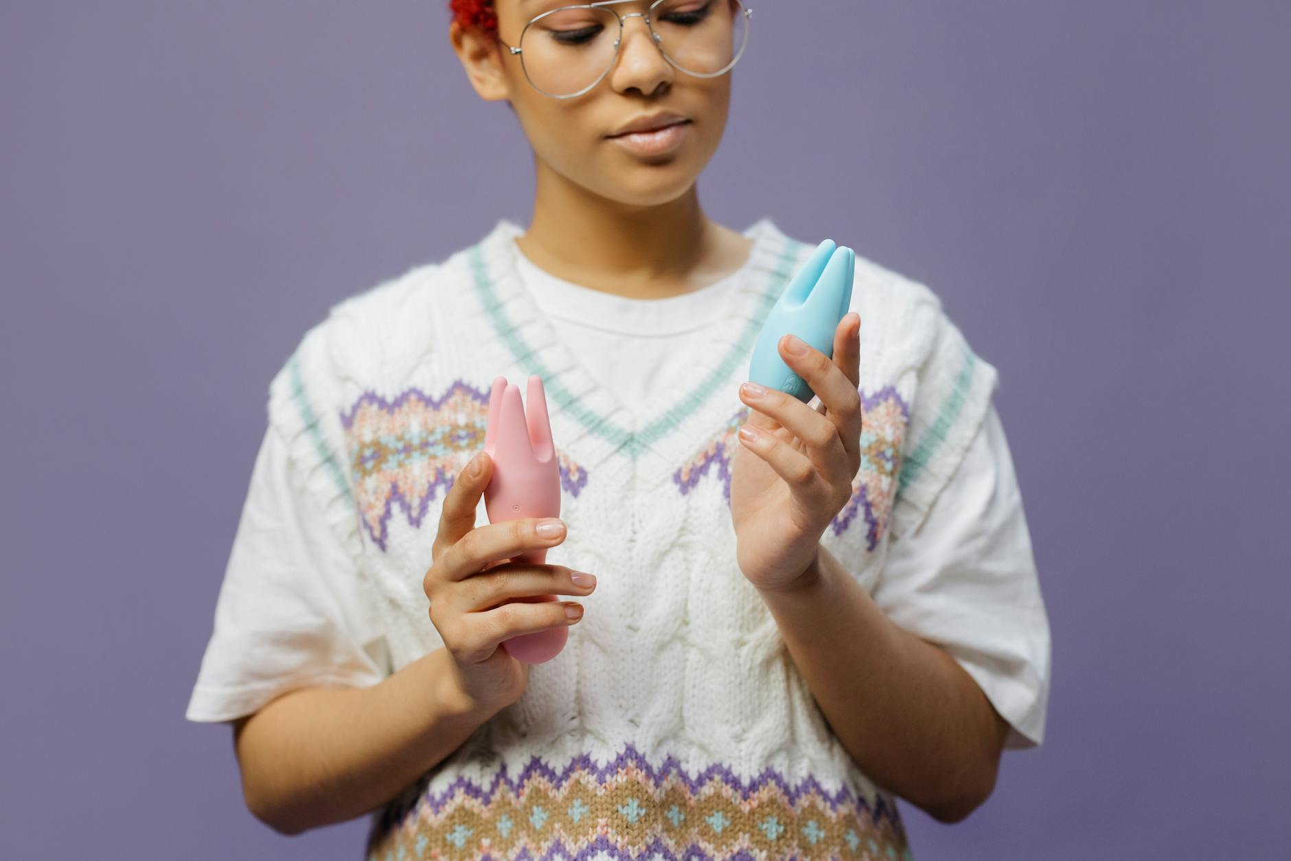 A woman holding a blue and pink silicone clitoral vibrator with a thoughtful expression