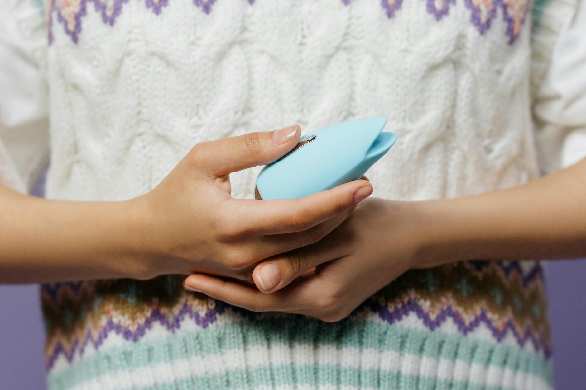 Manos sosteniendo un vibrador azul de silicona contra un fondo lavanda