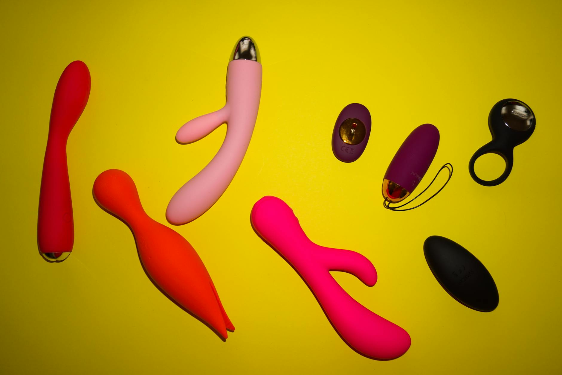 Colección de vibradores coloridos y juguetes sexuales exhibidos en una superficie amarilla brillante