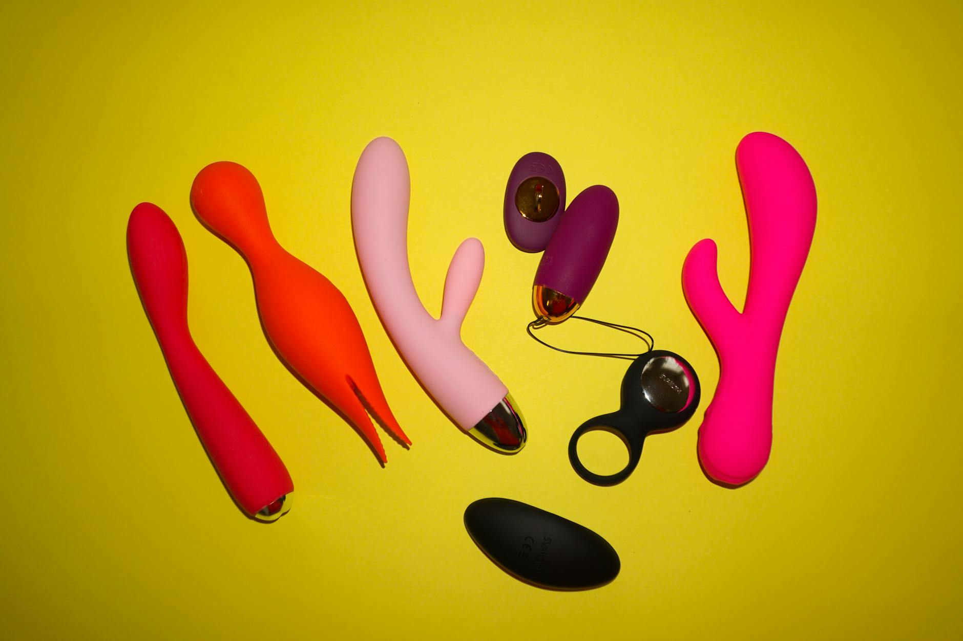 Colorful vibrators and personal massagers arranged on a bright yellow background